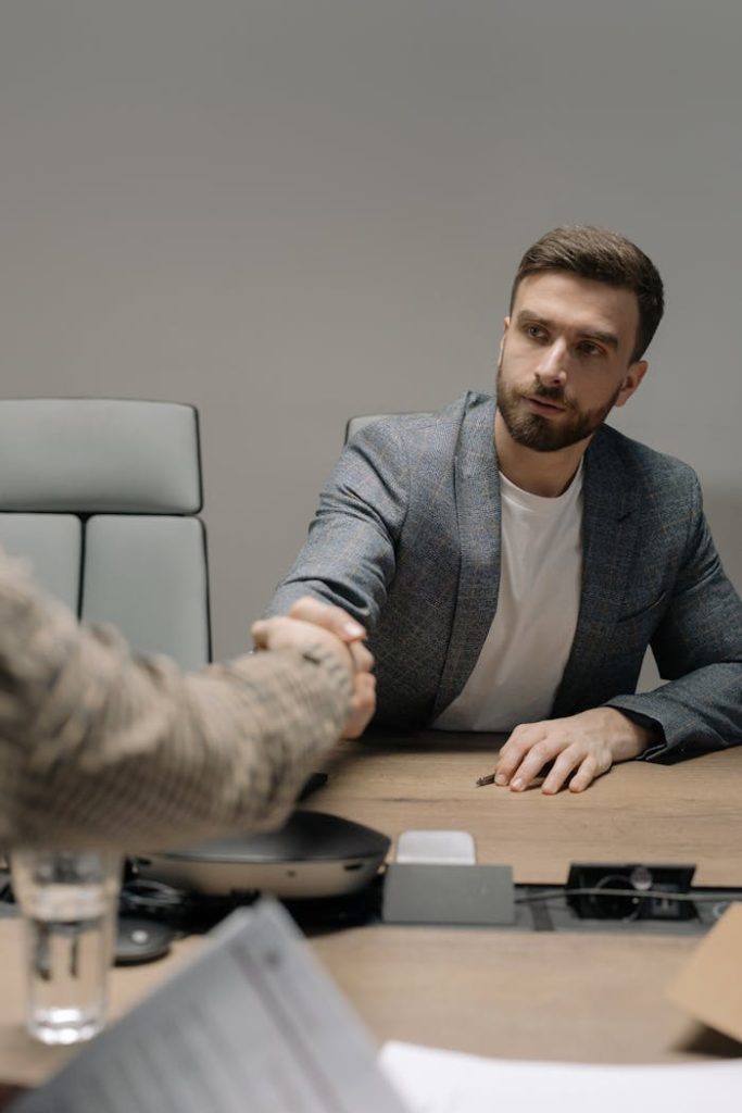 businessmen-shaking-hands-6814528 Two businessmen in a modern office shaking hands across a table. Professional setting.